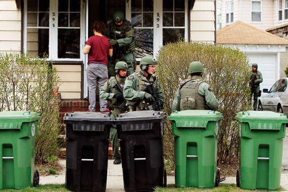 Residents watch as police officers search house to house for the second suspect in the Boston Marathon bombings in a neighborhood of Watertown