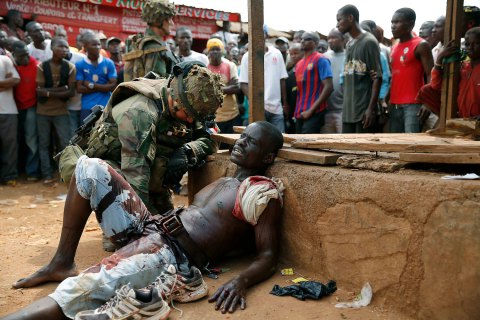 A French soldier speaks to suspected Christian militia member Sincere Banyodi, 32,  who lays wounded by machete blows in the Kokoro neighborhood of Bangui, Central African Republic, Monday  Dec. 9, 2013.   Vigilante crowds said they spotted him with grenades and turned him to French forces. Both Christian and Muslim mobs went on lynching sprees as French Forces deployed in the capital. French forces fired warning shots to disperse the crowds. (AP Photo/Jerome Delay)