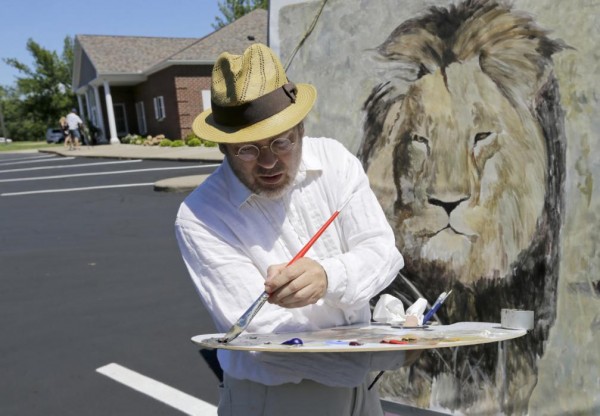 Mark Balma works on a mural of Cecil the lion outside Dr. Walter James Palmer's dental office in Bloomington, Minn., Wednesday, July 29, 2015. Authorities allege that Palmer paid $50,000 to track and kill Cecil, a protected lion, just outside Hwange National Park in Zimbabwe. (AP Photo/Ann Heisenfelt)