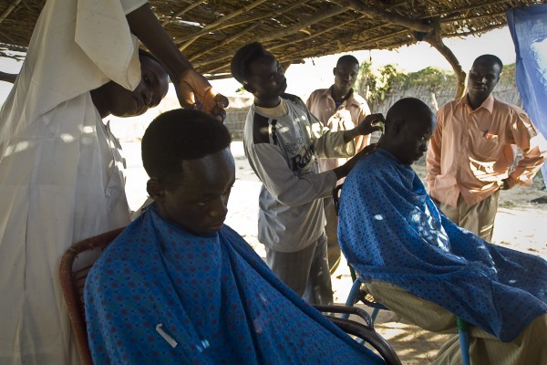 Barbers cutting the hair of clients in a makeshift barbershop built with bamboo and straw in Gaga refugee camp, Chad. Photo © European Commission