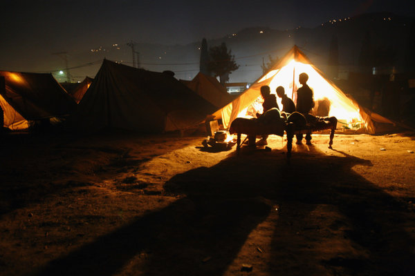 MUZAFFARABAD, PAKISTAN - DECEMBER 18: Earthquake survivors sit by their tent, which has electricity, in a small tented camp on December 18, 2005 in the devastated city of Muzaffarabad, Pakistan. Lack of snow is giving the quake survivors a break but they are still struggling in over crowded tented camps while fighting the cold weather with a shortage of winterized shelter. (Photo by Paula Bronstein /Getty Images)