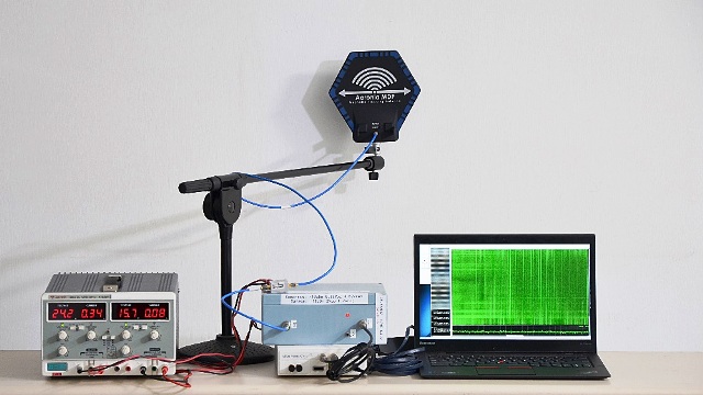 Image Source: IARC - Attacker's setup for capturing EM emanations. Left to right: power supply, antenna on a stand, ampliers, software dened radio (white box), analysis computer.