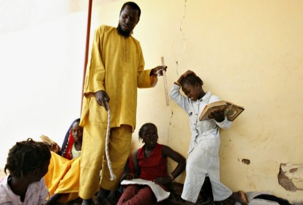 A girl winces in pain after being hit on the head with a stick by her instructor at a Koranic school on the outskirts of Senegal's capital Dakar